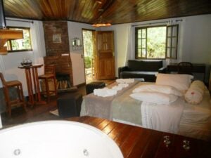 Interior do chal&eacute; com banheira redonda e cama de casal e varanda ao lado na Pousada Jardim das &Aacute;guas em Visconde de Mau&aacute;