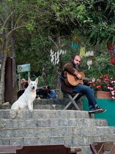 Homen sentado tocando violão e cão ao lado