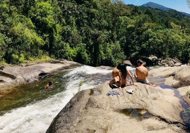 Pessoas sentadas ao lado do rio de uma cachoeira em Visconde de Maua