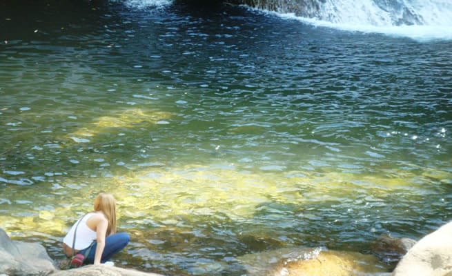 Mulher colocando a mão na água da cachoeira