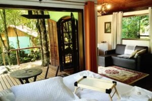 Cama de casal e sala ao fundo do chal&eacute; em Visconde de Mau&aacute;.