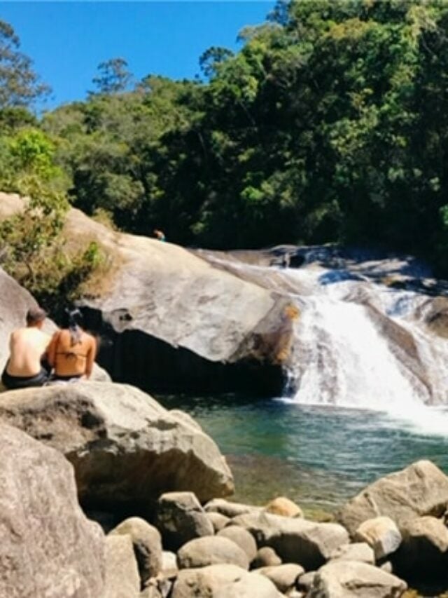 Casal sentado na pedra em frente a cachoeira