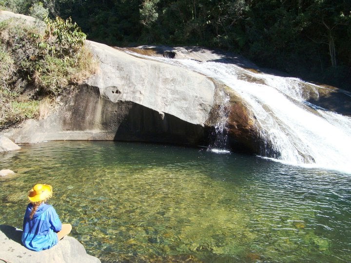 Mulher de chapéu sentada ao lado do rio em visconde de maua