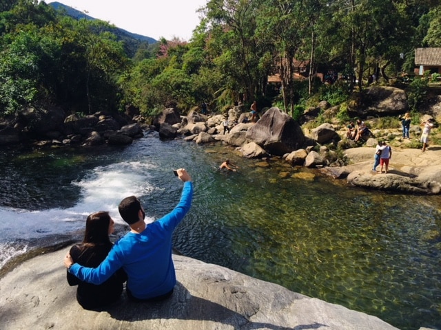 Casal abraçado sentado ao lado da cachoeira