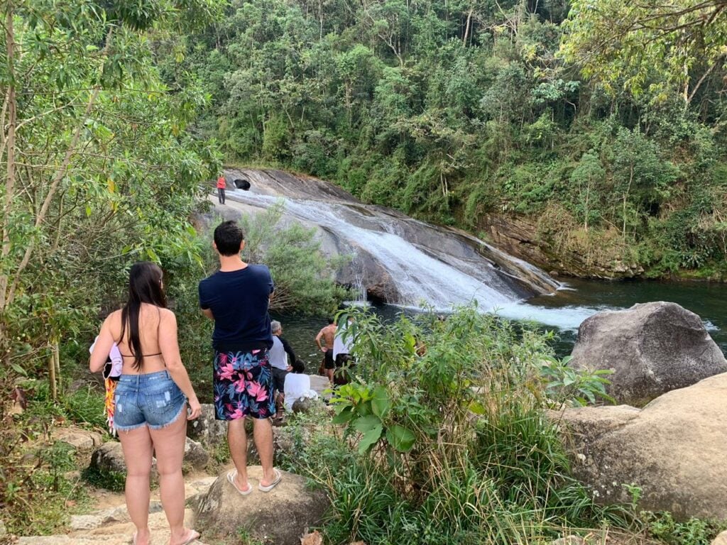 Casal na trilha para a cachoeira ao fundo em Visconde de Mauá