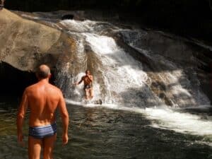Homem de costas de sunga e uma pessoas deslizando no rio de Visconde de Mauá