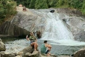 Casal sentado na pedra ao lado da cachoeira