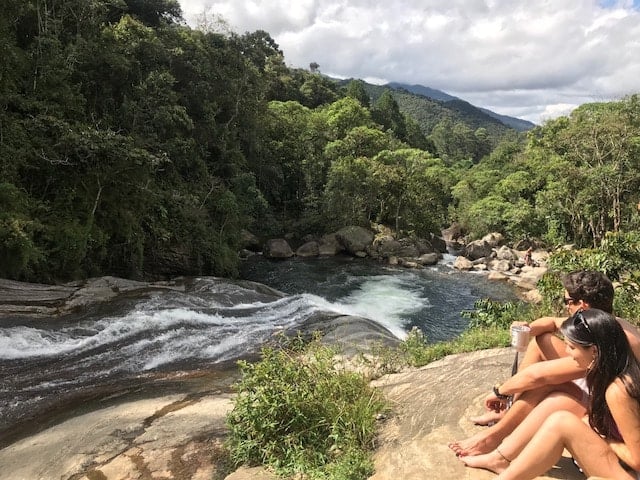 Casal sentado na margem da cachoeira em Visconde de Mauá