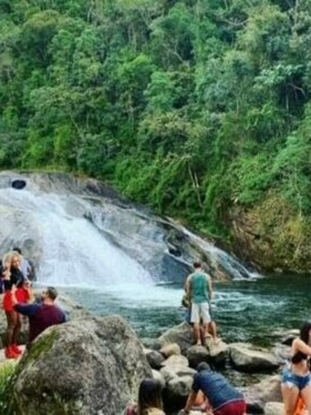 Pessoas sentadas nas pedras em torno de uma cachoeira de Visconde de Mauá