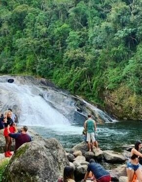 Pessoas sentadas nas pedras em torno de uma cachoeira de Visconde de Mauá