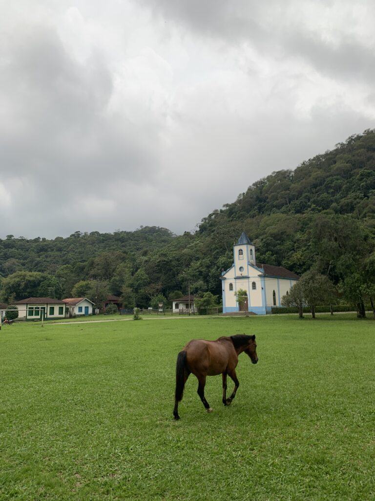 Vila de Visconde de Mauá, RJ com sua Igreja principal com um cavalo em meio a grama verde da montanha