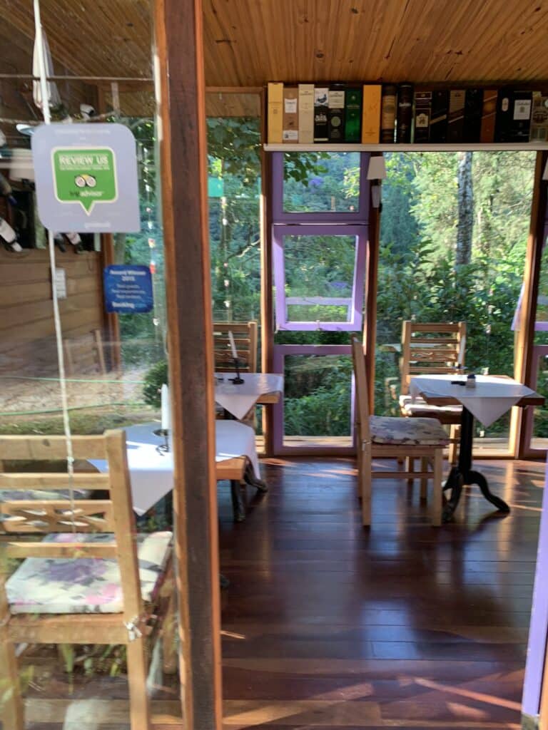 Sala envridraçada com mesas e vista da mata serrana